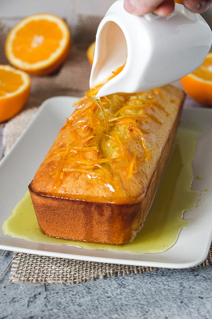 Pouring fresh orange syrup with zest over an orange loaf