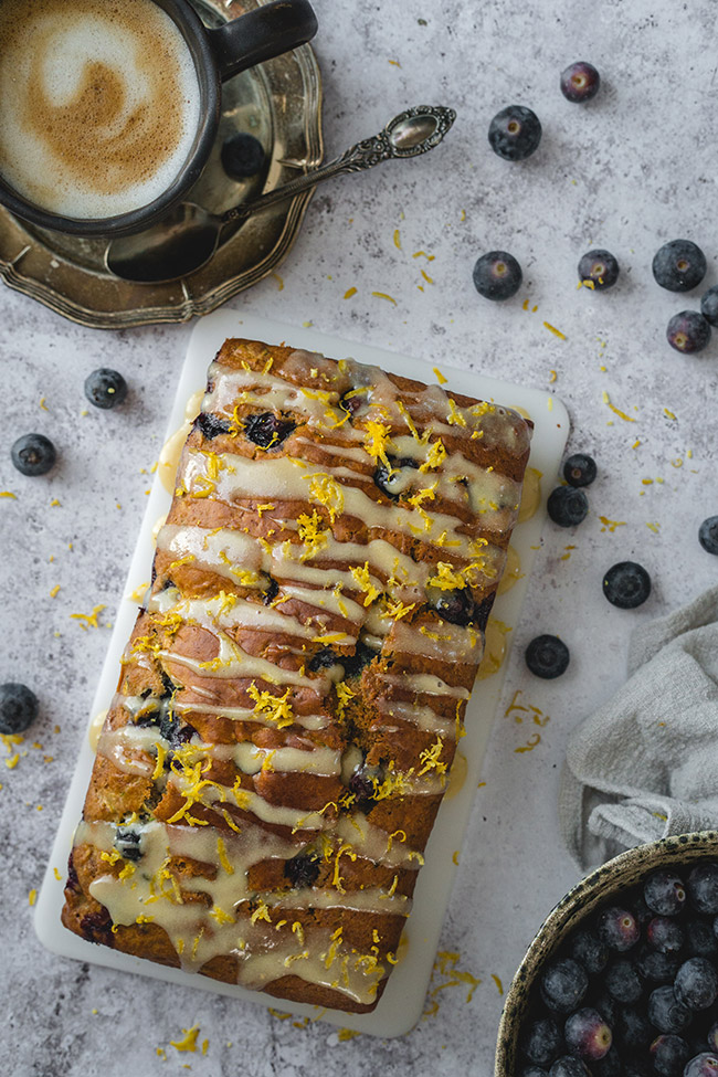 A loaf of a blueberry zucchini bread drizzled with a cashew lemon glaze