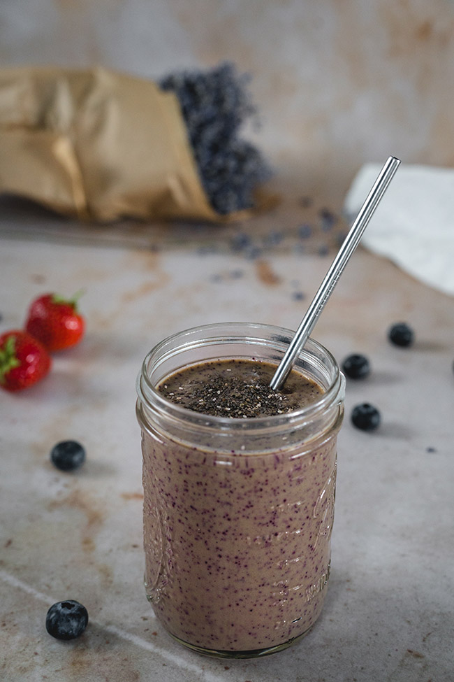 strawberry and spinach smoothie in a mason jar with a metal straw on a tiled background with scattered blueberries
