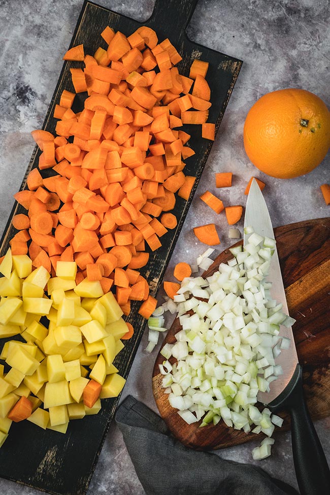 Chopped carrots, potatoes, and onions on a cutting board
