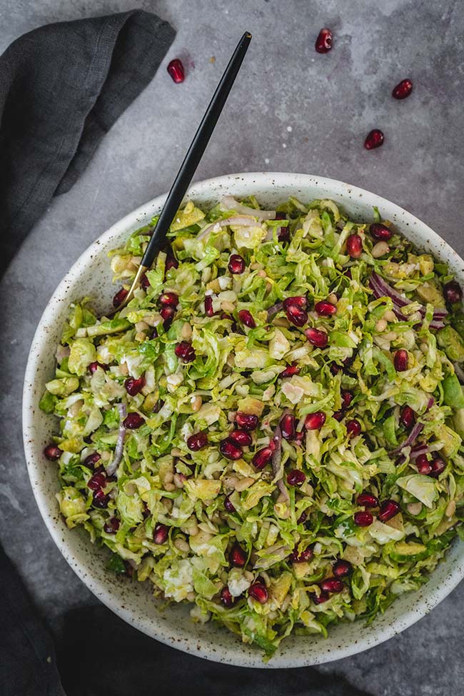 Brussels sprout pomegranate salad with feta cheese, red onion, and pine nuts in a bowl