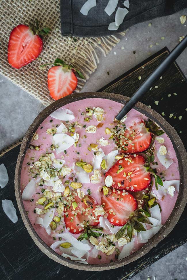 Strawberry banana smoothie bowl topped with coconut flakes, hemp seeds and pistachios overhead shot